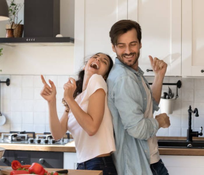 Overjoyed young family having fun in modern kitchen, dancing and laughing, happy young wife and husband moving to favorite music, enjoying leisure time, cooking dinner together, romantic date